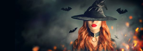عکس دختر جادوگر هالووین زن جوان زیبا در کلاه جادوگر با موهای قرمز موی قرمز و لب های روشن بیش از حوادث پس زمینه جنگل سحر و جادو تاریک تاریک طراحی هنری حزب هالووین