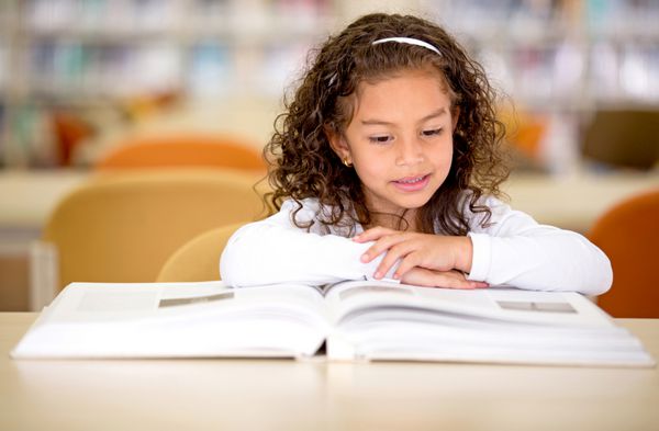دختر مدرسه ای جوان خواندن یک کتاب در کتابخانه
