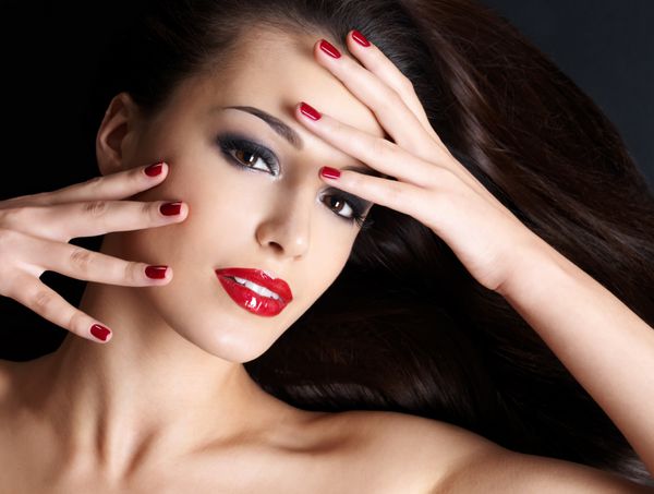 زن زیبا با موهای بلند قهوه ای مستقیم و ناخن های قرمز دروغ گفتن در پس زمینه تاریک