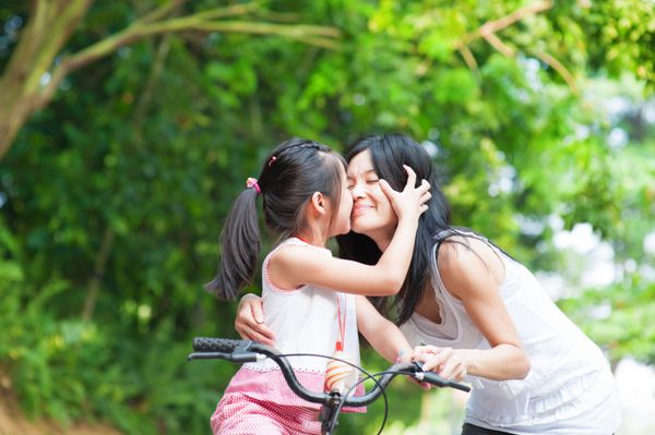 کودک آسیایی بوسیدن مادرش خانواده آسیایی سرگرم کننده در فضای باز دوچرخه سواری در فضای باز