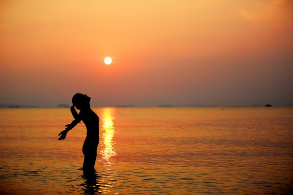 زن دست باز در زیر طلوع آفتاب در دریا