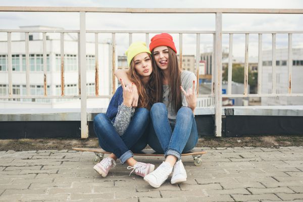 دو دختر جوان جوان longboarding نشسته در هیئت مدیره طولانی و لذت داشتن خارج از منزل شیوه زندگی