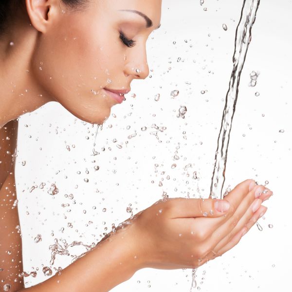 پرتره نزدیک از یک زن زیبا که تمیزش چهره پاکش را با آب دارد