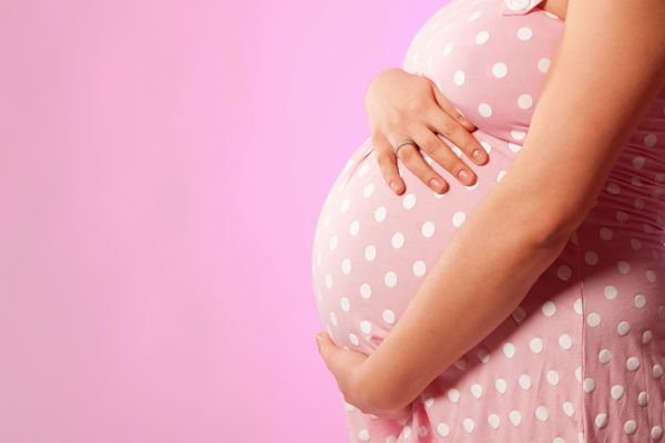 نزدیک شدن زن باردار غیر قابل تشخیص با دست بیش از شکم در پس زمینه صورتی