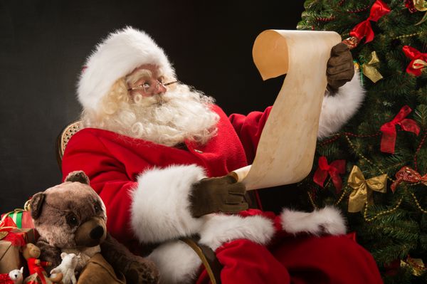 پرتره از بابا نوئل نشسته در اتاق خود را در خانه در نزدیکی درخت کریسمس و کیسه بزرگ و خواندن نامه کریسمس و یا لیست آرزو