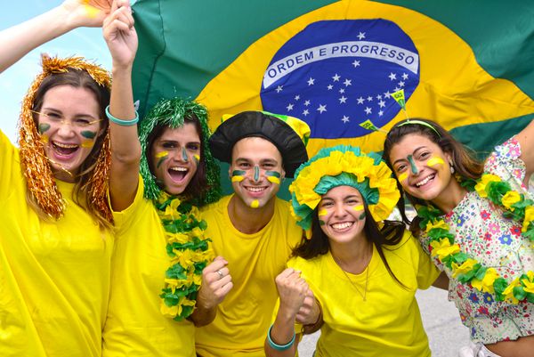 گروهی از طرفداران فوتبال برزیل در پی پیروزی با پرچم برزیل در حال حرکت در هوا هستند