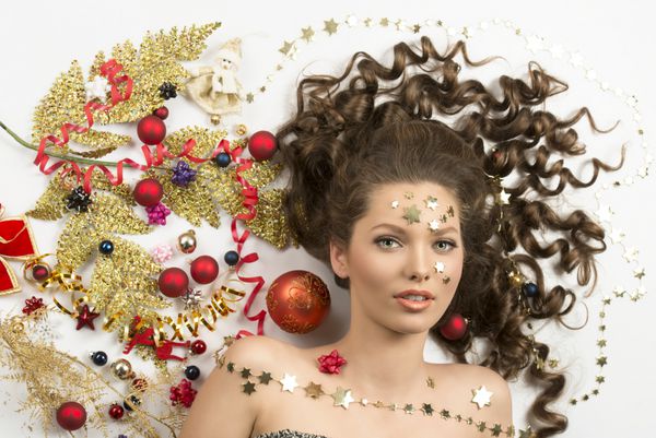 مفهوم کریسمس پرتره نزدیک از زن ناز زیبا با احاطه توسط دکوراسیون کریسمس رنگارنگ baubles قرمز شاخه طلایی روبان و ستاره در چهره او