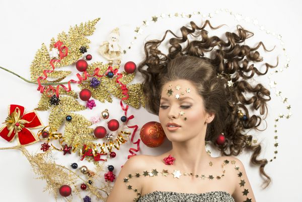 دختر جوان دروغ گفتن با موی بلند قهوه ای قرمز و شانه های مختلف دکوراسیون کریسمس خنده دار احاطه شده است بی رنگ قرمز و رنگارنگ روبان ستاره های طلایی و شاخه xmas خلاقانه