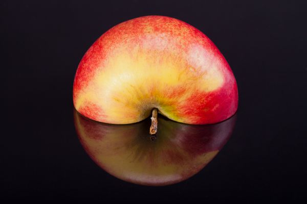 نیمی از سیب سرخ با بازتاب جدا شده در پس زمینه سیاه و سفید
