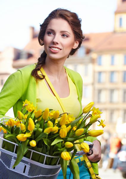 زن با پوشیدن یک دامن بهار مانند یک پیراهن با دوچرخه با چند گل زرد در سبد در شهر قدیمی نگهداری می کند