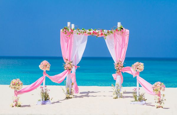 قوس عروسی تزئین شده با گل در ساحل شن و ماسه استوایی تنظیم عروسی ساحل در فضای باز