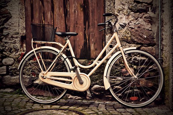 دوچرخه زرد ایتالیایی قدیمی با سبک قبلی با سبد خرید در مقابل یک دیوار گرانج در زیر یک درخت چوبی ایستاده است