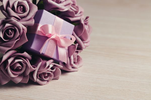 گلهای بنفش و جعبه هدیه با روبان صورتی روی سطح چوبی