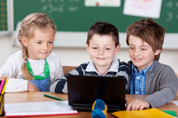 سه دانش آموز جوان یک دختر بسیار کوچکی و دو پسر با استفاده از یک لپ تاپ در کلاس نشسته با هم در یک میز