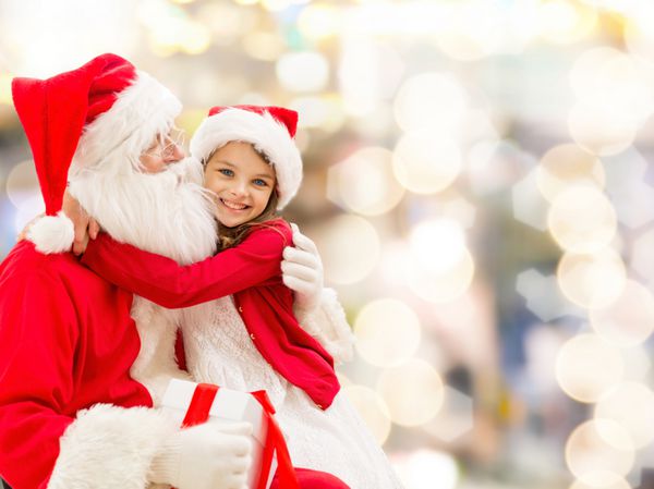 تعطیلات کریسمس دوران کودکی و مفهوم مردم لبخند زدن دختر کوچک در آغوش با سانتا کلاوس در زمینه چراغ