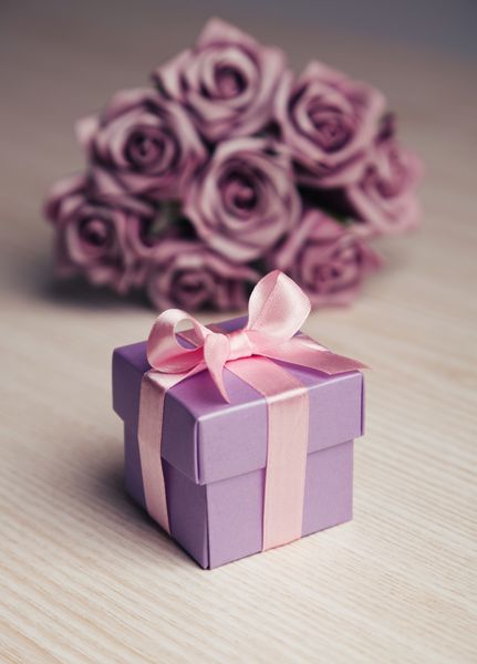 گل رز بنفش و جعبه هدیه با روبان صورتی روی سطح چوبی