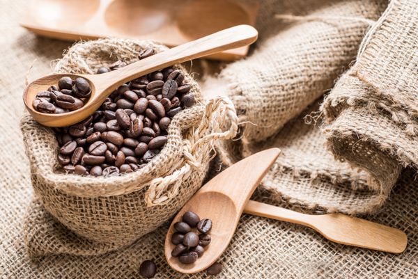 دانه های قهوه در کیسه های قهوه ساخته شده از خاکستری در سطح کیسه