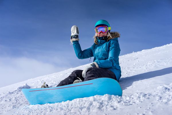 شاد زن جوان snowboarder نشسته در شیب برفی به اسنوبورد در معبد اسکی در اسکله است