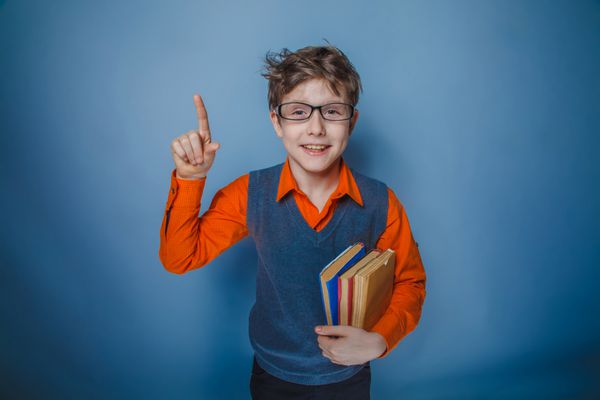 نوجوان پسر با کتاب های ظاهر اروپا با عینک انگشت خود را لبخند زد در پس زمینه خاکستری یکپارچهسازی با سیستمعامل شادی