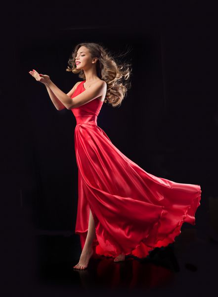 زن زیبای جوان در لباس قرمز تکان دادن پرواز در لباس ابریشمی