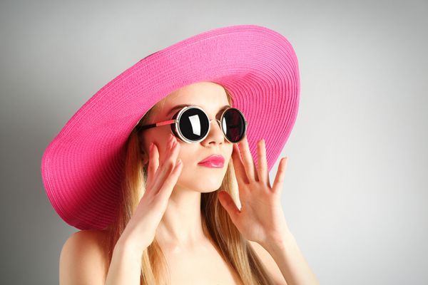 مدل ابرقهرمان جوان در کلاه صورتی با عینک آفتابی در پس زمینه خاکستری