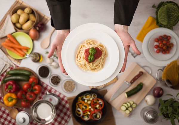 سرآشپزهای حرفه ای دست پخت و پز را بر روی یک میز کار چوبی با سبزیجات مواد غذایی و ظروف نمایش بالا دست می دهند