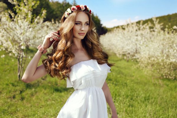 مد عکس در فضای باز از زن زیبا با موی قرمز طولانی و گل بشکه در باغ شکوفه بهار