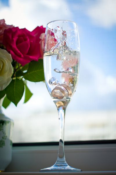 حلقه های عروسی در شیشه ای با شامپاین در برابر آسمان آبی