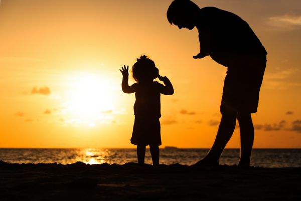 سایه های پدر و دختر کوچک در ساحل در غروب آفتاب