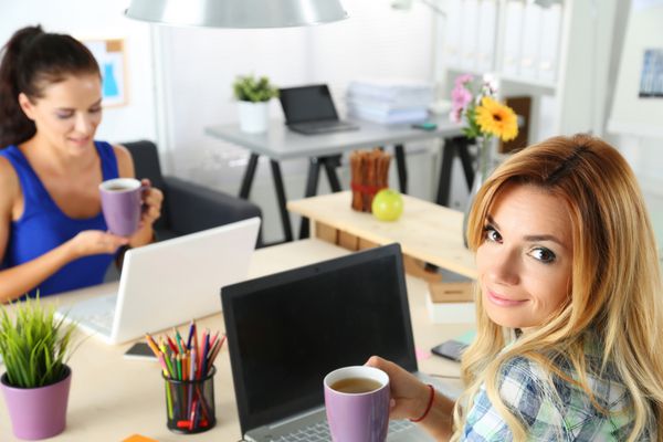 دو طراح زن در دفتر نوشیدن چای صبحانه یا قهوه کافئین در طول روز سخت کار می کند زن کارمند نگه داشتن فنجان نوشیدنی افراد خلاق یا مفهوم کسب و کار تبلیغاتی