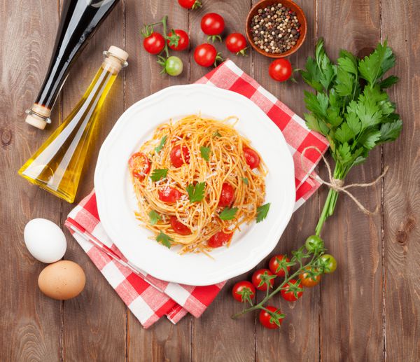 ماکارونی اسپاگتی با گوجه فرنگی و جعفری روی میز چوبی نمای بالا
