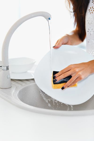 بستن دست مانیکور شده از زن جوان شستن ظروف سفالی در سینک آشپزخانه با استفاده از اسفنج با فوم صابون