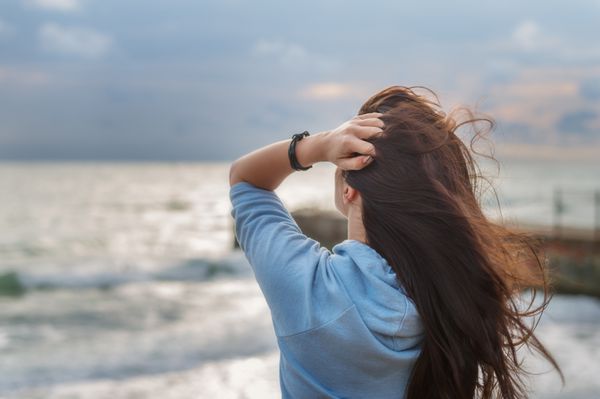 دختر با موهای طولانی تیره در پس زمینه از دریا و آسمان آبی