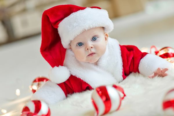 کودک خندان که دراز کشیدن بر روی شکم پوشیدن کلاه بابا نوئل کریسمس قرمز و سفید و کت و شلوار جدا شده در پس زمینه سفید