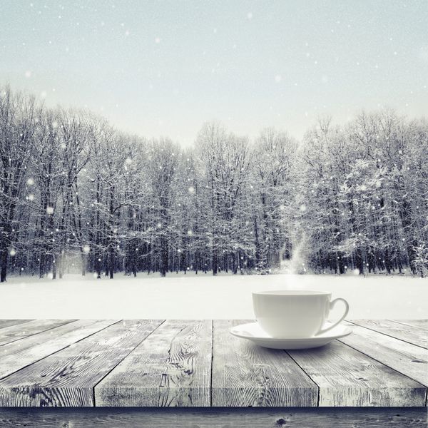 نوشیدنی در فنجان بر روی میز چوبی بر روی زمستان برف تحت پوشش جنگل پس زمینه زیبایی طبیعت