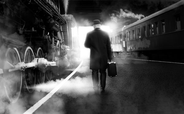 عکس سیاه و سفید مرد در لباس های پرنعمت راه رفتن در ایستگاه راه آهن قدیمی