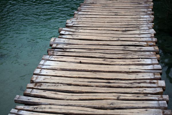 عکس نزدیک از مسیر چوب پلکان پل چوبی ساخته شده از تخته های چوبی در سراسر آبی سطح دریاچه آبی سبز با موج در روز در زمینه چشم انداز طبیعی تصویر افقی