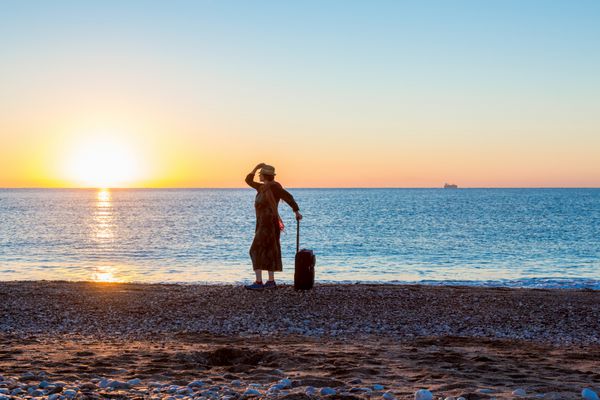 افراد مفهومی تعطیلات ساحلی زنانه Silhouette ماندن در امتداد ساحل اقیانوس با کیسه چمدان لذت بردن از منظره دریا و طلوع آفتاب در پس زمینه