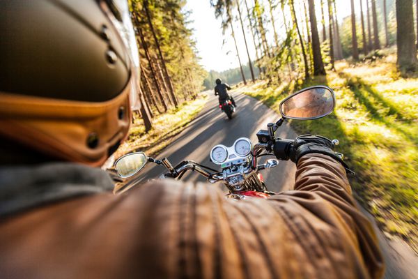 صندلی مرد در موتور سیکلت در جاده جنگل در طلوع آفتاب