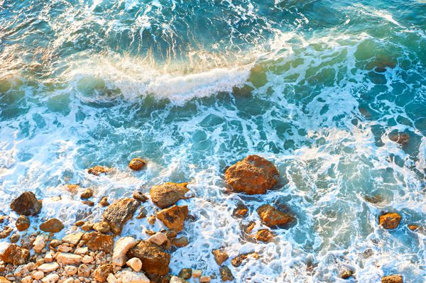 موج در یک ساحل سنگی در غروب آفتاب دید هوایی