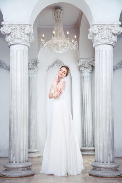 عروس جذاب در رشد کامل در لباس طولانی در سالن با ستون