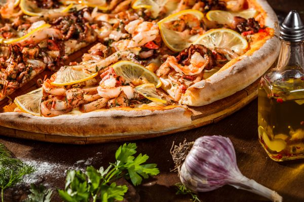 پیتزا ایتالیایی با لیمو پنیر و غذاهای دریایی در پس زمینه میز چوبی روستایی تصویر Closeup