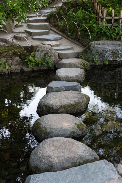 مسیر زین سنگ در یک باغ ژاپنی در یک حوض آرام در اوکایاما