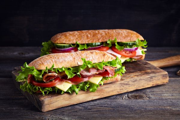 دو ساندویچ زیردریایی تازه با ژامبون پنیر بیکن گوجه فرنگی کاهو خیار و پیاز در تخته های چوبی