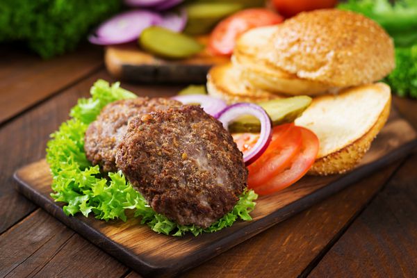 مواد لازم برای ساندویچ برگر همبرگر با گوشت گاو ترشی گوجه فرنگی و پیاز قرمز در زمینه های چوبی