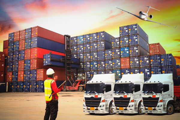 کانتینر صنعتی کامیون حمل و نقل کالا برای مفهوم Logistics Import Export لجستیک تجاری حمل و نقل کانتینر حمل و نقل با کار جرثقیل پل در کارخانه کشتیرانی در غروب برای Logistic Import Export