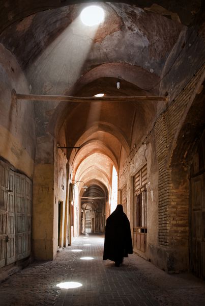 زن در حجاب راه رفتن را از طریق بازار قدیمی یزد روشن می کند با پرتو نور از دهانه های آسمان