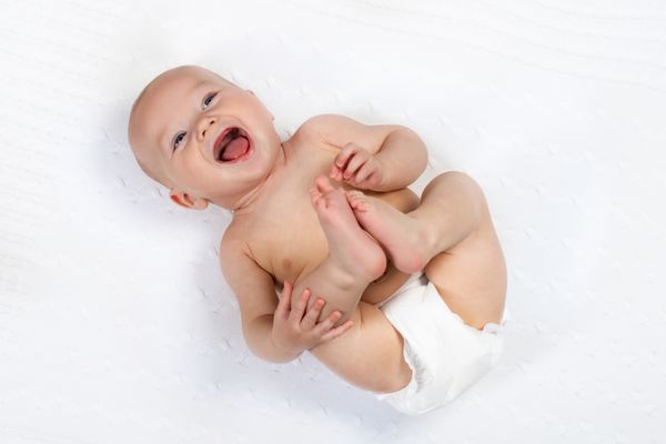یک بچه کوچک خنده دار یک پتو را روی یک پتو بافندگی سفید در یک مهد کودک آفتابی پوشید کودک پس از حمام یا دوش در یک حوله تازه تغذیه تغذیه نوزادان و مراقبت از پوست بچه ناز با پای خود