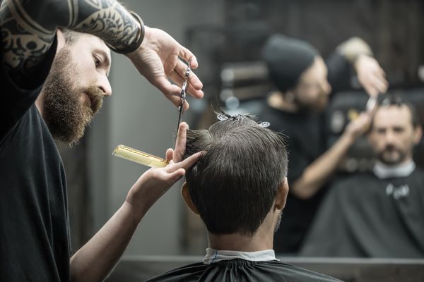 سلمانی بی نظیر با یک ریش بزرگ برش موی سر خود را از روی موی سیاه چاقو مو در آرایشگاه برش می دهد مشتری موهایش را روی سر قرار می دهد هر دو مبهم در آینه منعکس شده است