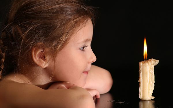 پرتره یک دختر 4-5-6 سال به دنبال شمع سوختن جدا شده بر روی زمینه سیاه است